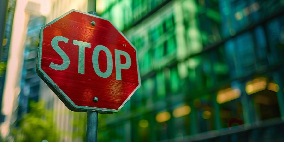 Foto eines großen Glas-Firmengebäudes im unscharfen Hintergrund mit einem deutlich sichtbaren Stop-Schild im Vordergrund.